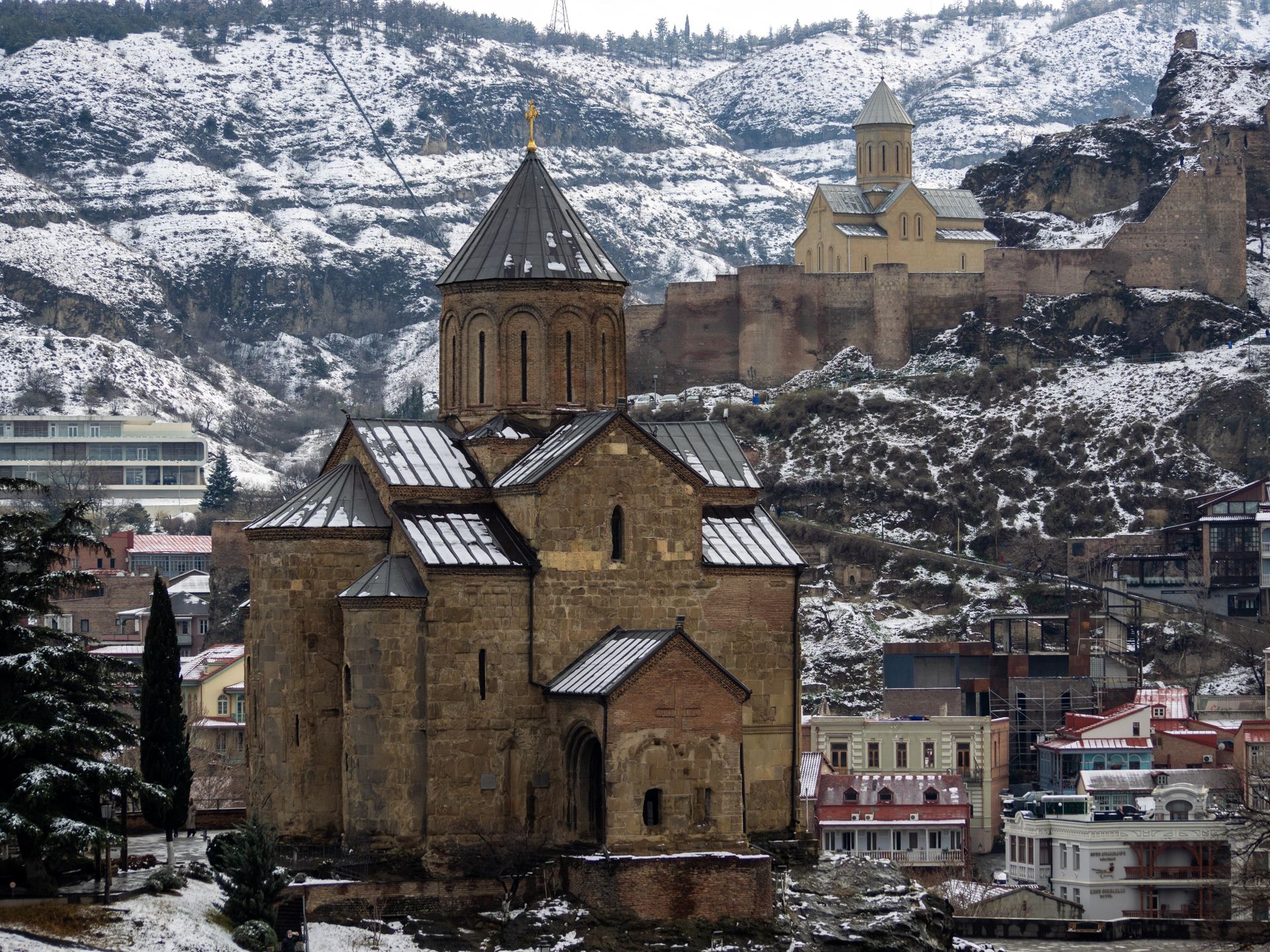 A snowy view of the historical Metekhi St Virgin Church and Narikala Fortress in Tbilisi, Georgia.