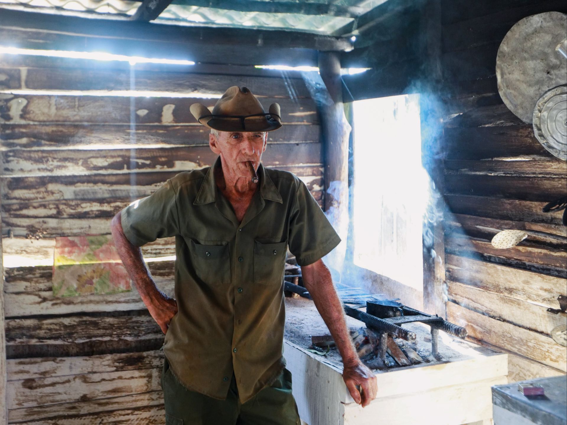 Elderly cowboy in a rustic wooden cabin, enjoying a smoke in daylight.