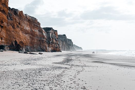 Expansive sandy beach with towering cliffs and gentle sea waves, perfect for nature lovers.