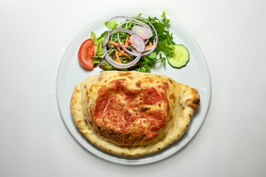 A delicious calzone served with a fresh vegetable salad on a white plate. Perfect for food photography.