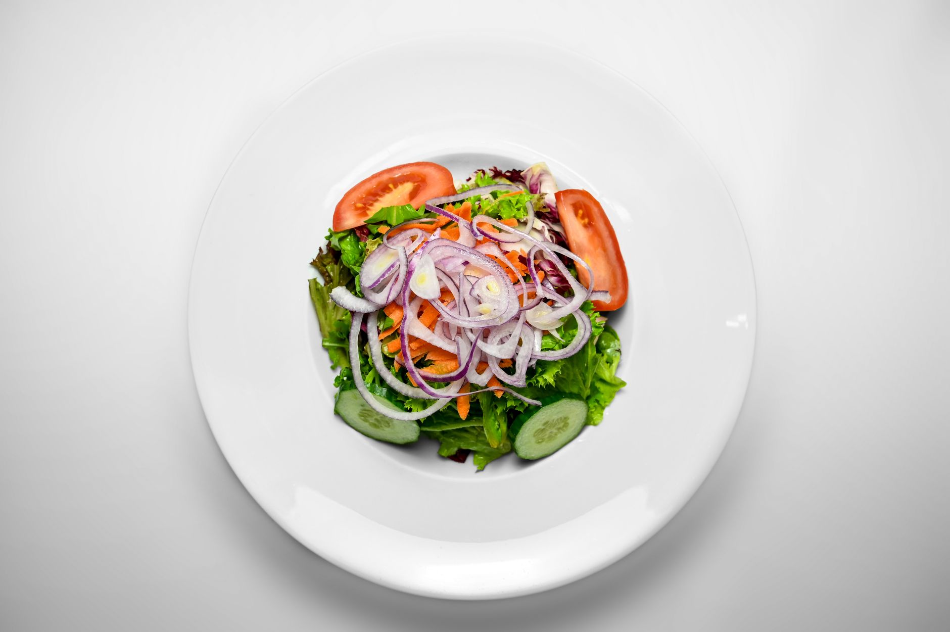45 Easy Vegetable Side Dishes for Every Occasion Overhead view of a fresh garden salad with sliced onions, tomatoes, and cucumbers on a white plate.
