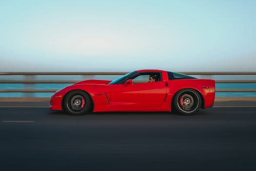 Vibrant red sports car cruising on a bridge with ocean in the background, captured in Kuwait.