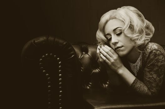 A vintage-style portrait of a woman with blonde hair lounging on a leather couch in a sepia tone.