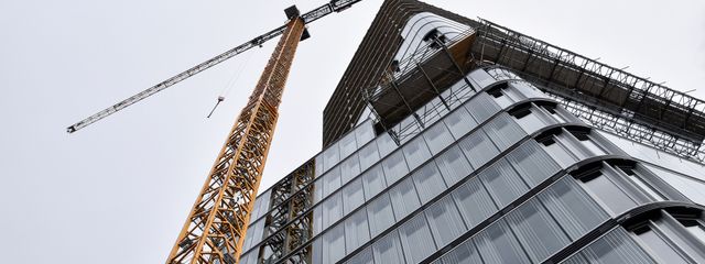 A low angle shot of modern building under construction with a crane viewed against the sky.