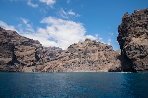 Free Stunning rocky cliffs rise above a vibrant blue sea under a clear sky, capturing nature's raw beauty. Stock Photo