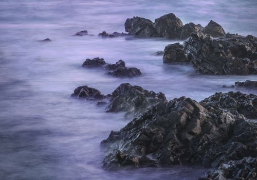 Free Calm ocean waves over rocks at dusk, creating a serene and tranquil coastal scene. Stock Photo