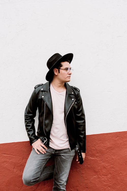Free Man in Eyeglasses Standing at Wall in Black Hat and Leather Jacket Stock Photo