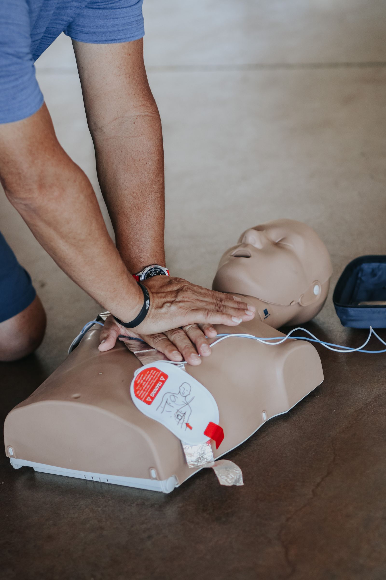 Hands demonstrating resuscitation on a training mannequin beside a defibrillator
