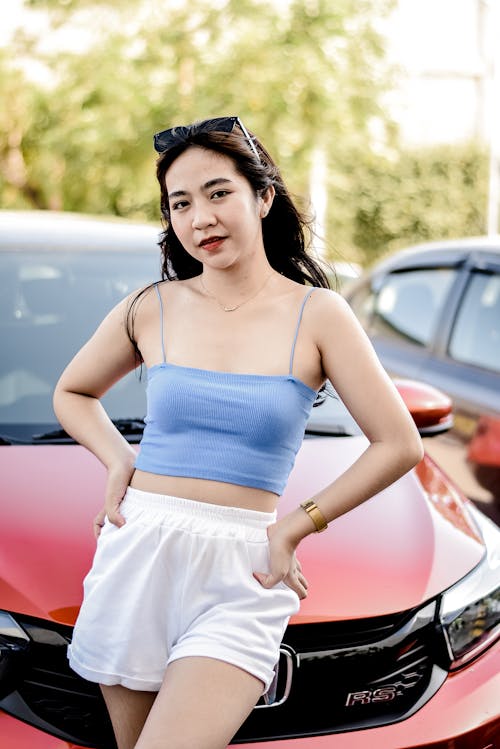 A Woman in Blue Spaghetti Strap Top and White Short Standing Beside Red Car