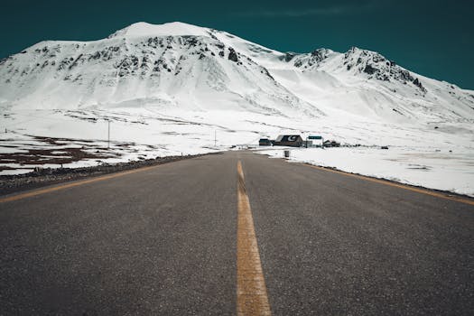 Picturesque winter road leading to snow-covered mountains under a clear sky.