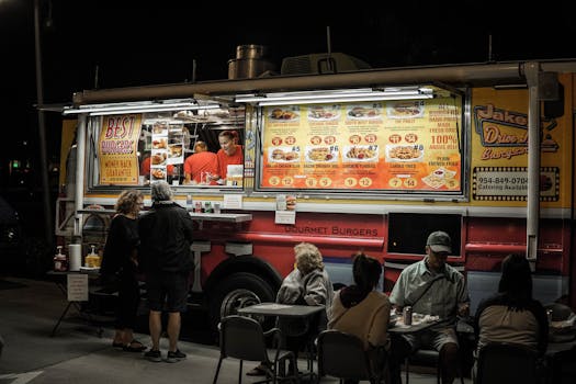 Food truck serving gourmet burgers at night with customers ordering and dining outdoors.