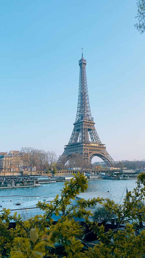 Free Eiffel Tower against a clear blue sky with the Seine River in Paris, a famous landmark. Stock Photo