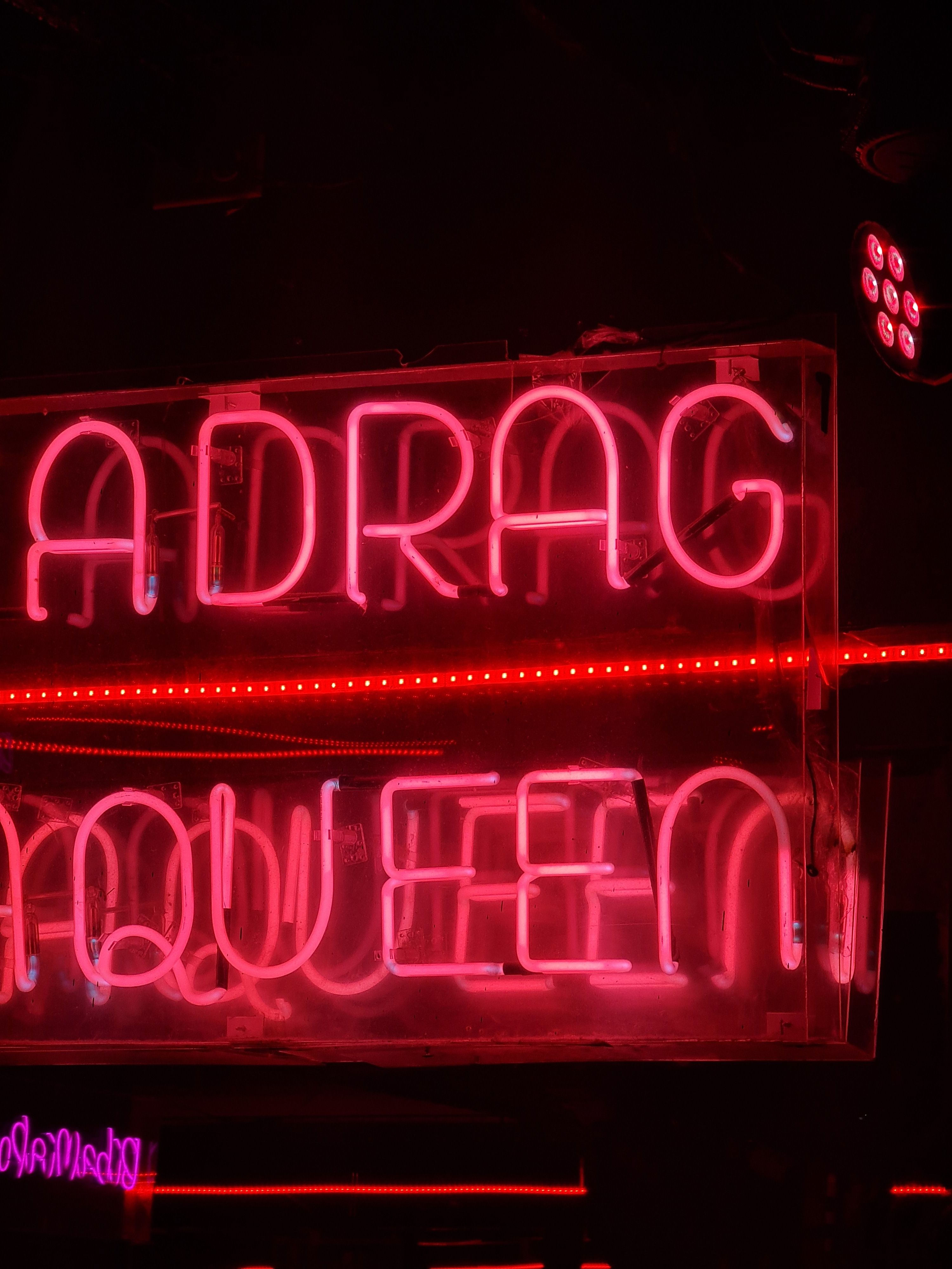 Close-up of neon sign with glowing pink letters spelling Drag Queen, creating a vibrant atmosphere.