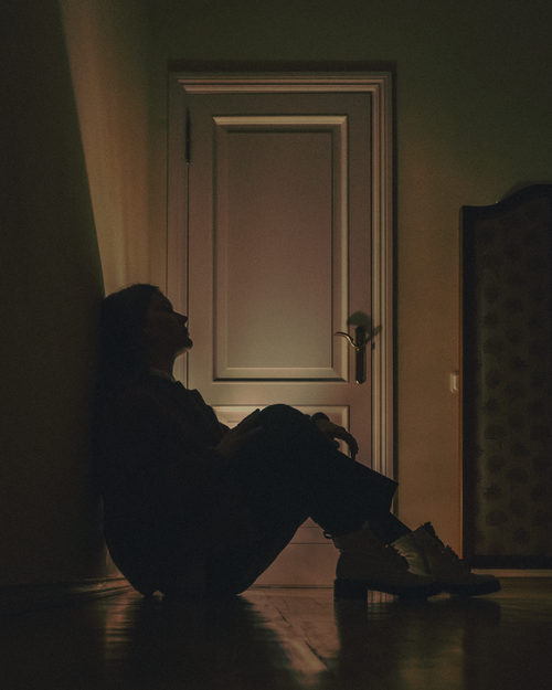 Free A silhouette of a woman sitting against a wall in a dimly lit room, conveying solitude and introspection. Stock Photo