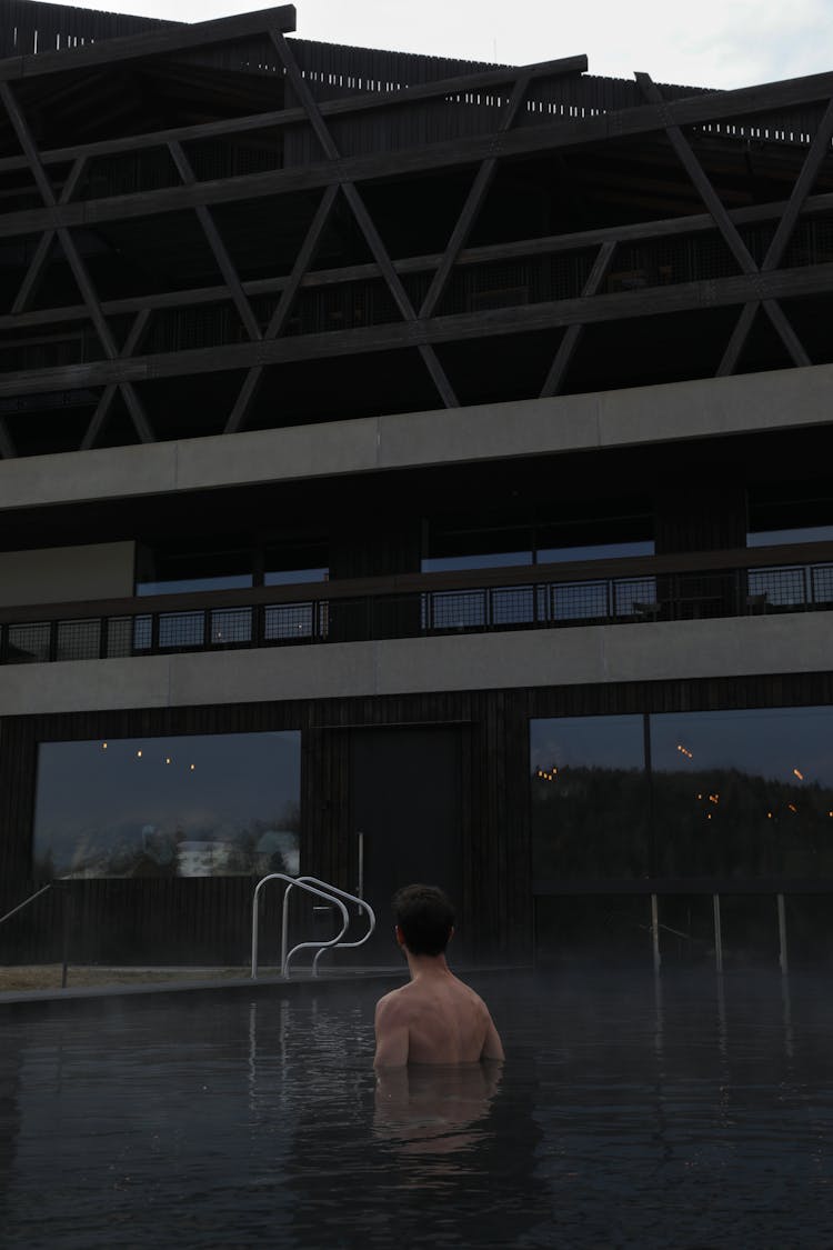 Man In Pool In Front Of Dark Facade Of House