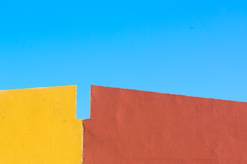 Free Bright yellow and red walls contrasting with a vivid blue sky in a minimalist style. Stock Photo