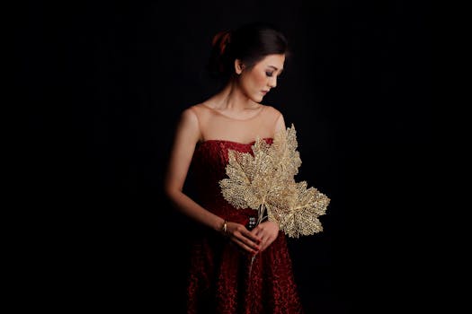 Portrait of a woman in a red dress holding golden leaves against a dark background.