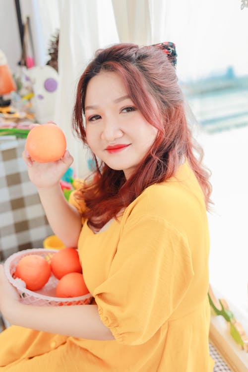 Free Woman in Yellow Shirt Holding Orange Fruit Stock Photo