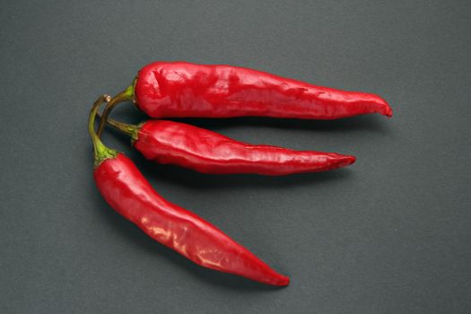 Close-up of three red chili peppers on a gray surface, showcasing their vibrant color and spicy nature.