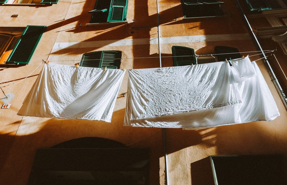 Sunlit white linens hang on a clothesline between buildings, casting shadows.