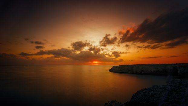 Breathtaking ocean sunset with dramatic clouds and serene reflection on the water.