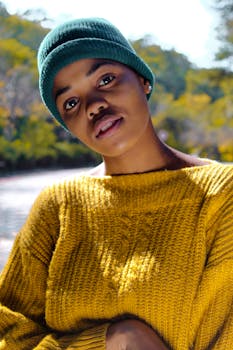 一位年轻女子穿着黄色针织毛衣，戴着绿色无檐小便帽，在户外的阳光下