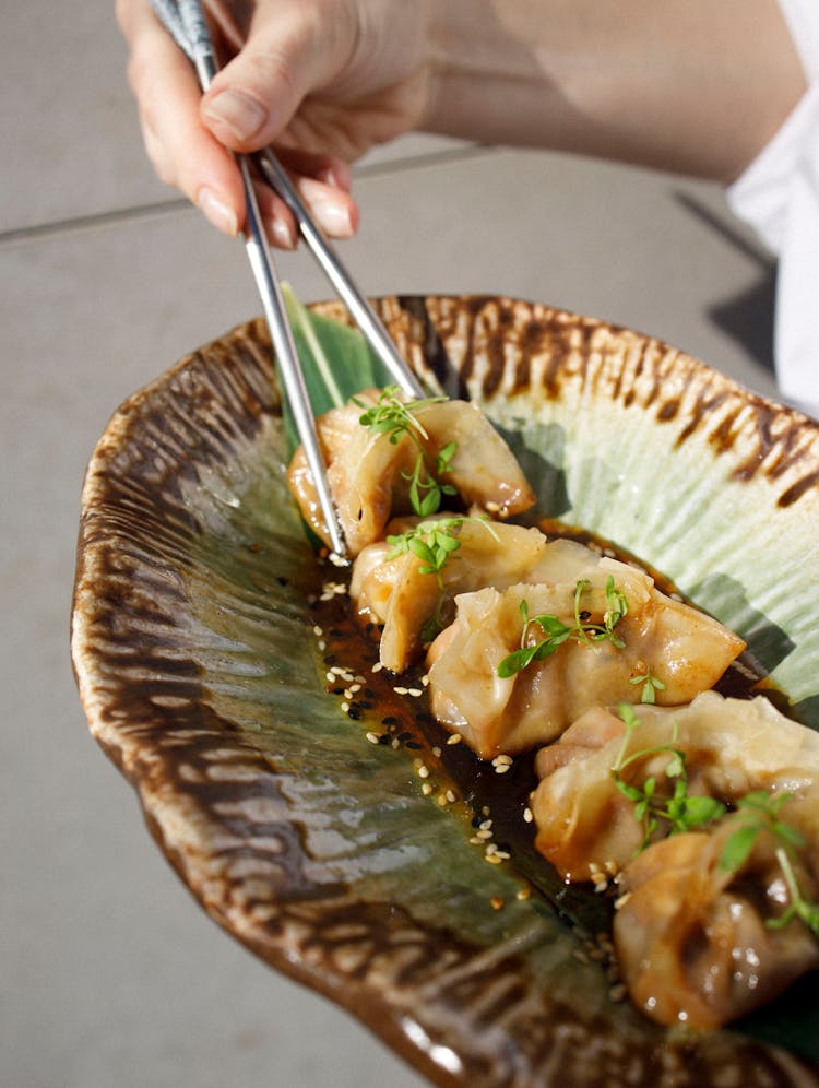 Person Eating Gyoza Dumplings With Chopsticks