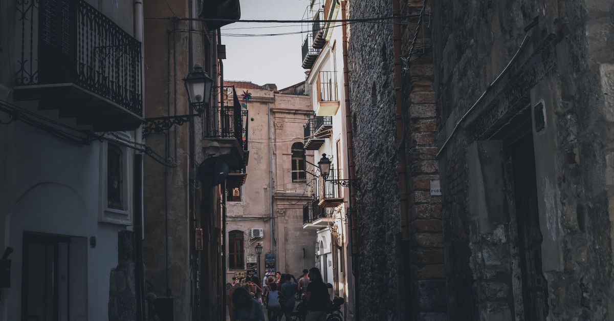 A person reading a book on a quiet balcony overlooking a narrow cobblestone street in Italy, morning light, no crowds