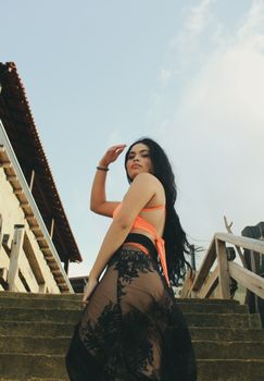 Elegant woman posing outdoors in a sheer skirt with blue sky backdrop.