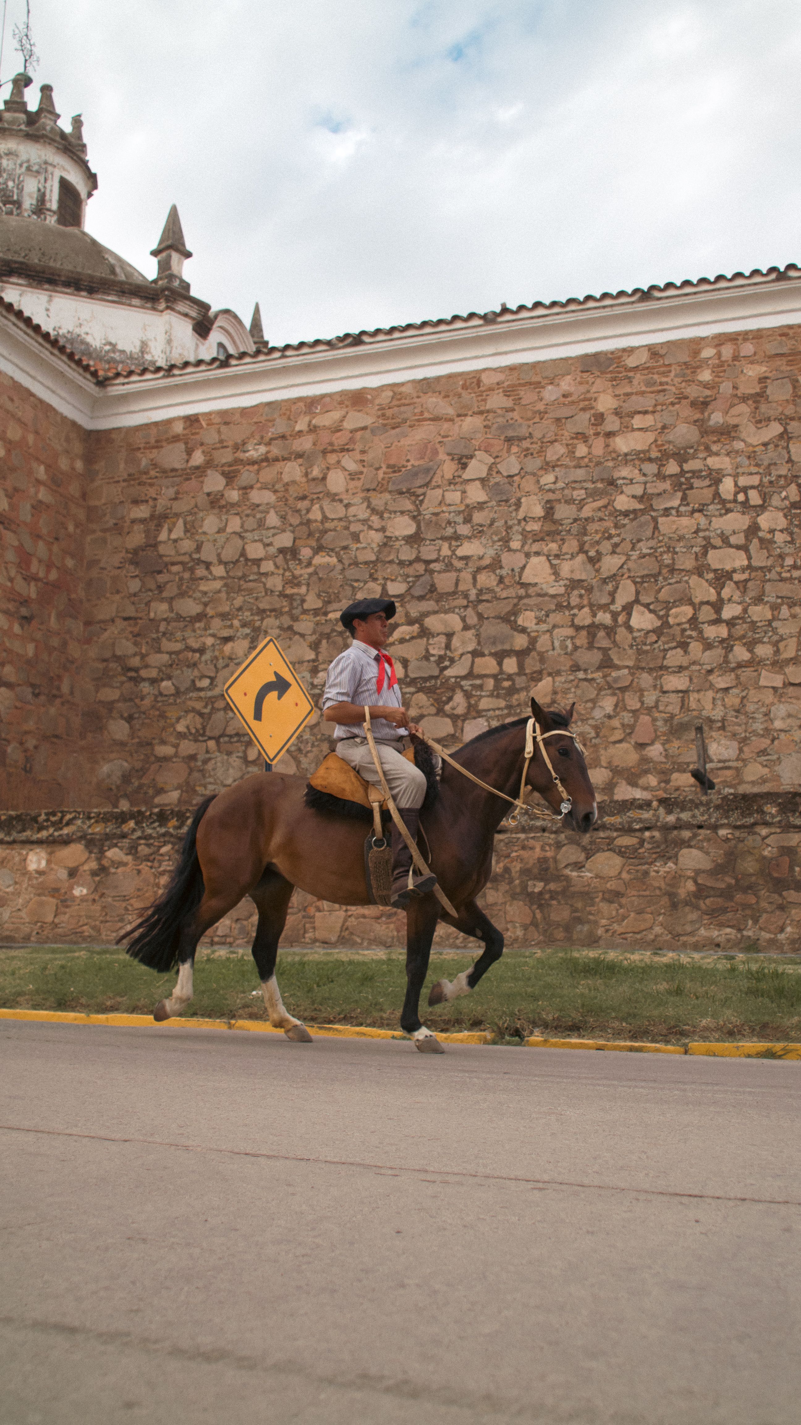 A gaucho on horseback rides past a stone wall in Argentina, showcasing traditional culture.