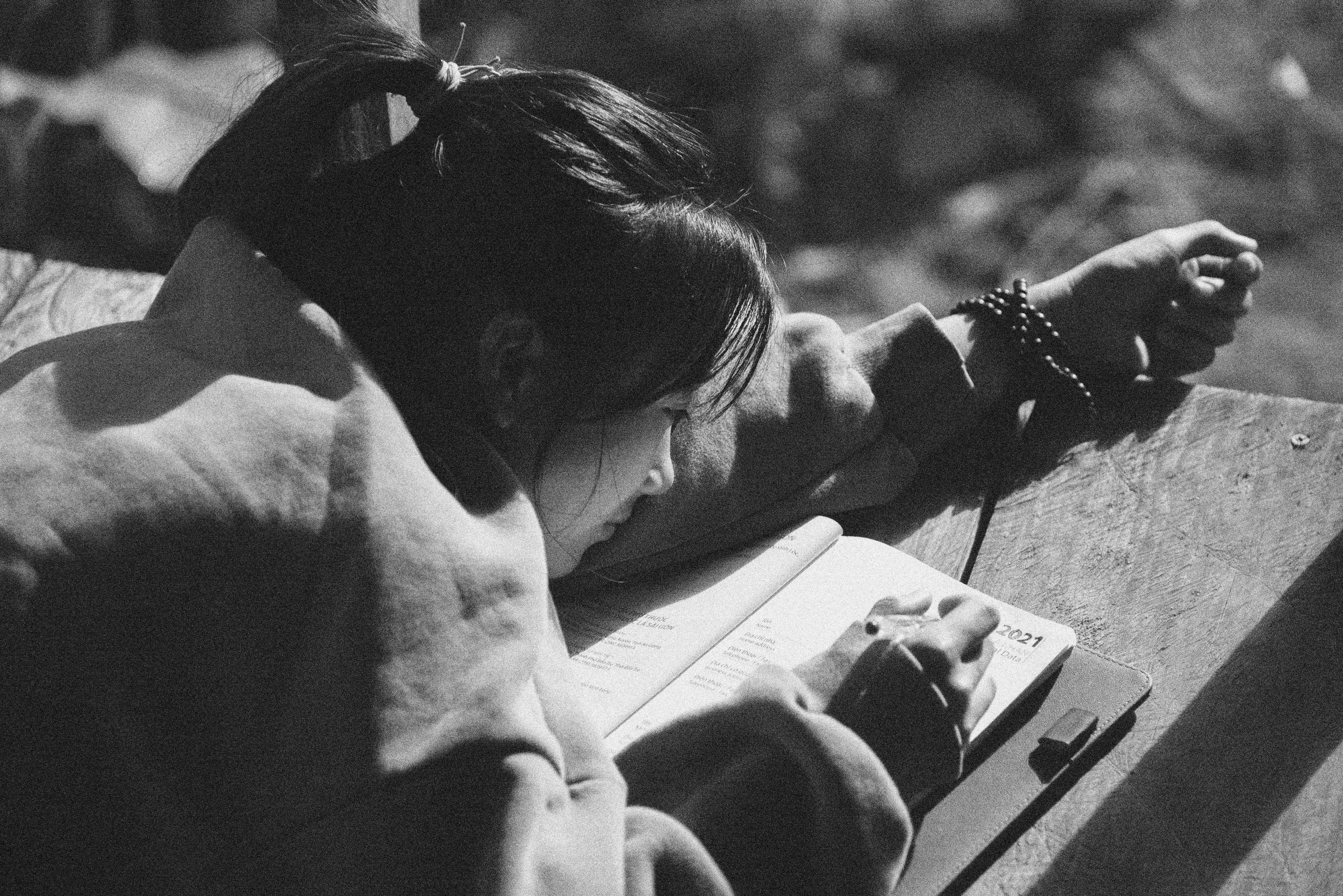 Black and white image of a woman writing in her journal on a sunny day.