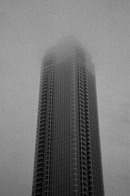 Monochrome image of a towering skyscraper engulfed in fog in Rotterdam, creating a surreal urban scene.