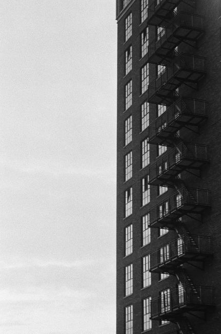 Black and white image of a tall building with fire escape stairs, showcasing modern architecture in Rotterdam.