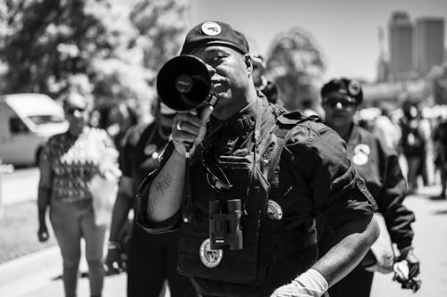 Grayscale Photo of a Policeman Talking using a Megaphone