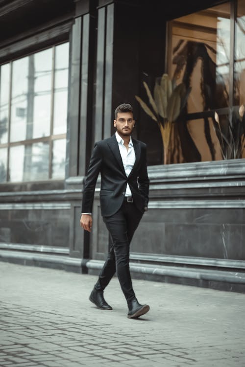A Man in Black Suit and Pants Walking on the Street