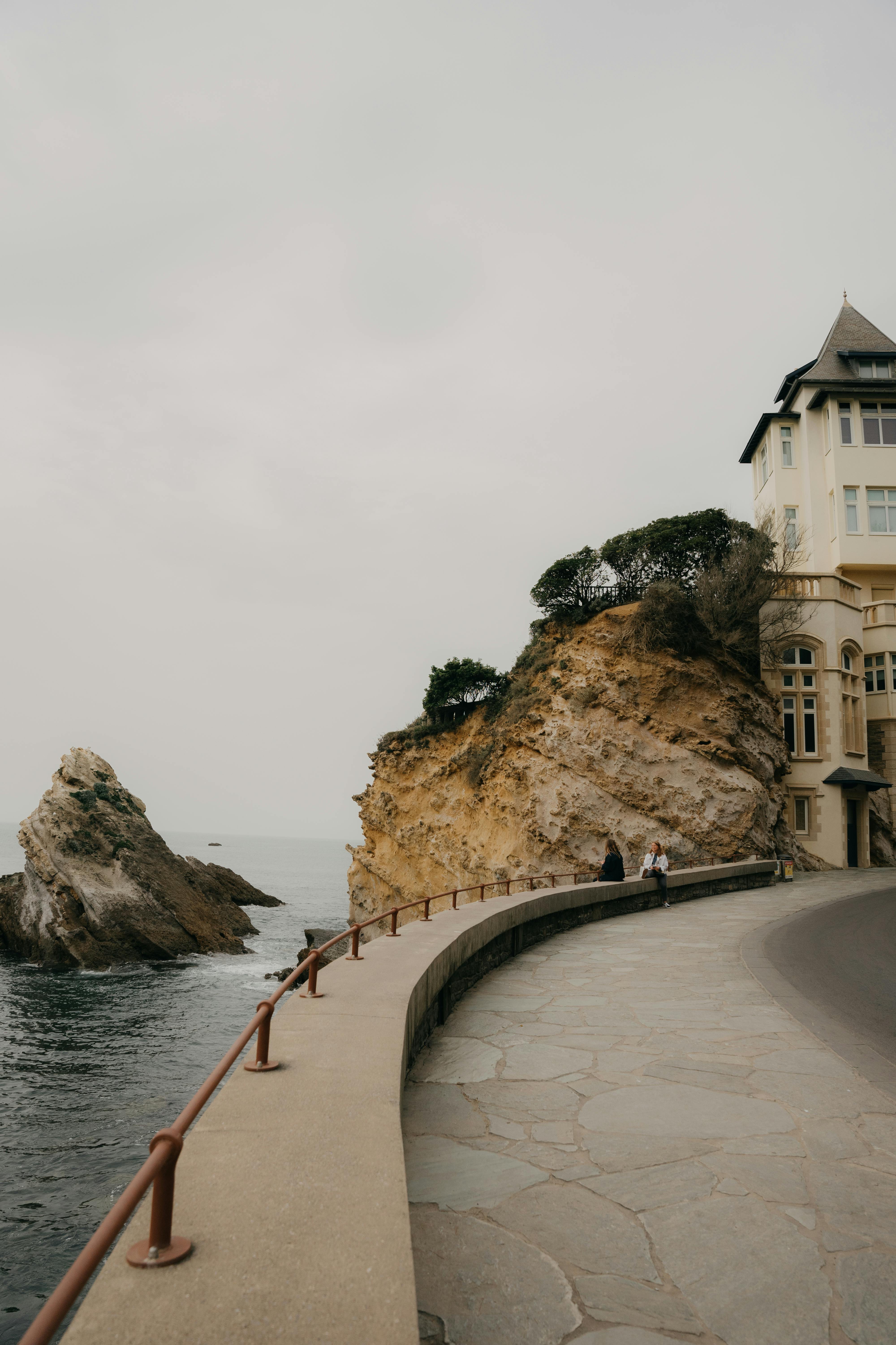 A serene view of a cliffside pathway along the Biarritz coastline with a historic building.