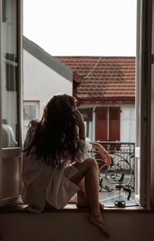 A woman sits on a windowsill in La Celle-sous-Gouzon, enjoying the morning sun.