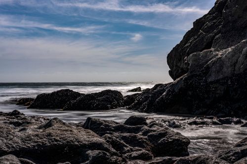 Free Dramatic rocky seaside view capturing waves and a vibrant blue sky. Stock Photo