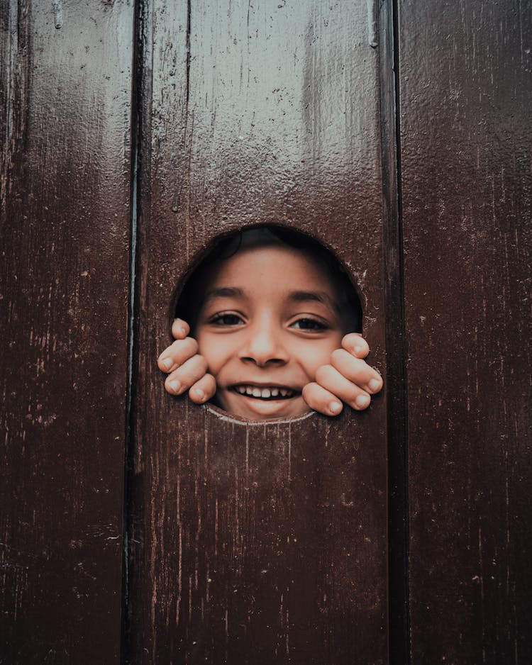 A Child Looking Through A Hole In The Fence