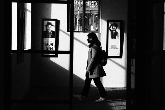 A woman walks through a gallery in Istanbul, showcasing light and shadow play in black and white.