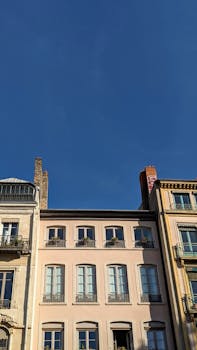 Charming historic building facades with tall windows and clear blue skies, perfect for urban architecture themes.