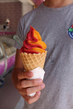 Close-up of a vibrant ice cream cone being held, showcasing swirled colors in a cozy indoor setting.