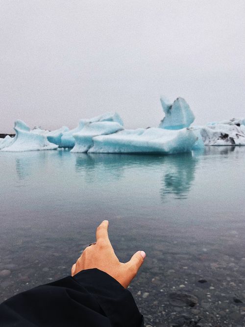 Free A hand reaches out over a serene Icelandic lake with floating icebergs under a cloudy sky. Stock Photo
