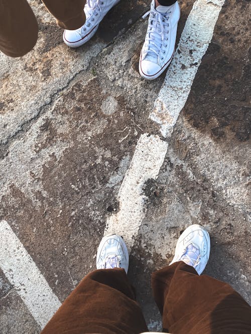 People Wearing White Sneakers Standing on Concrete Pavement