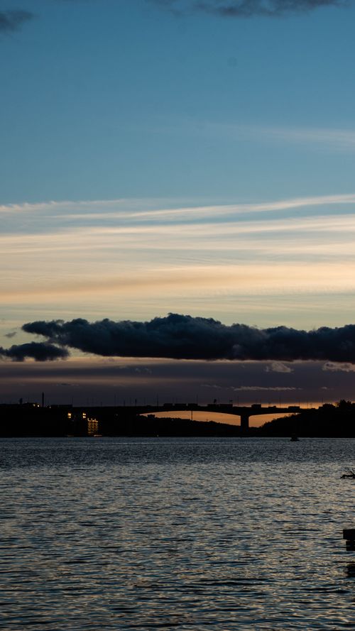 Free A tranquil view of a bridge at twilight with silhouetted clouds and calm waters. Stock Photo