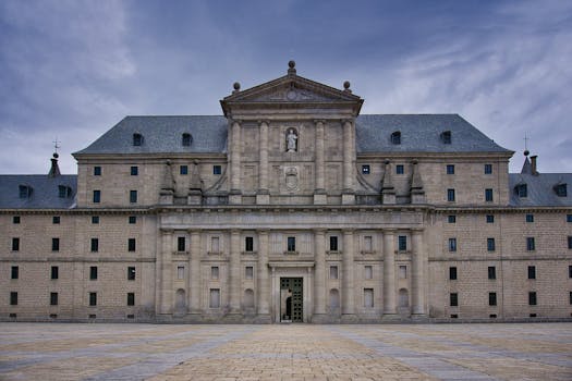 Majestic view of the San Lorenzo de El Escorial Monastery's facade under a cloudy sky.