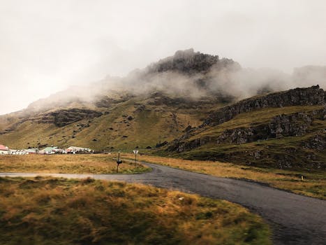 Scenic view of a foggy mountain and small village in Iceland's countryside, showcasing natural beauty and rural charm.
