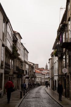 Cobblestone street in Spain lined with historic buildings and pedestrians on an overcast day.