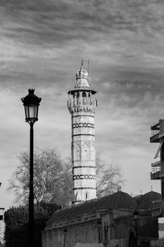 Black and white photo of a historic minaret in Adana, Turkey with a dramatic sky.