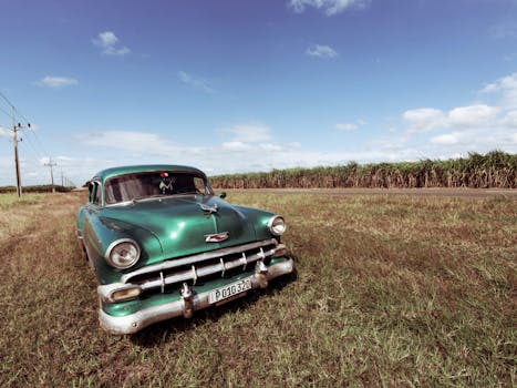 Retro green car parked in a grassy field under a cloudy sky, showcasing classic automotive elegance.